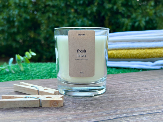 Fresh Linen scented candle by Hellomelts placed outdoors with folded towels and pegs, styled for a spring cleaning theme to promote freshness and home care.