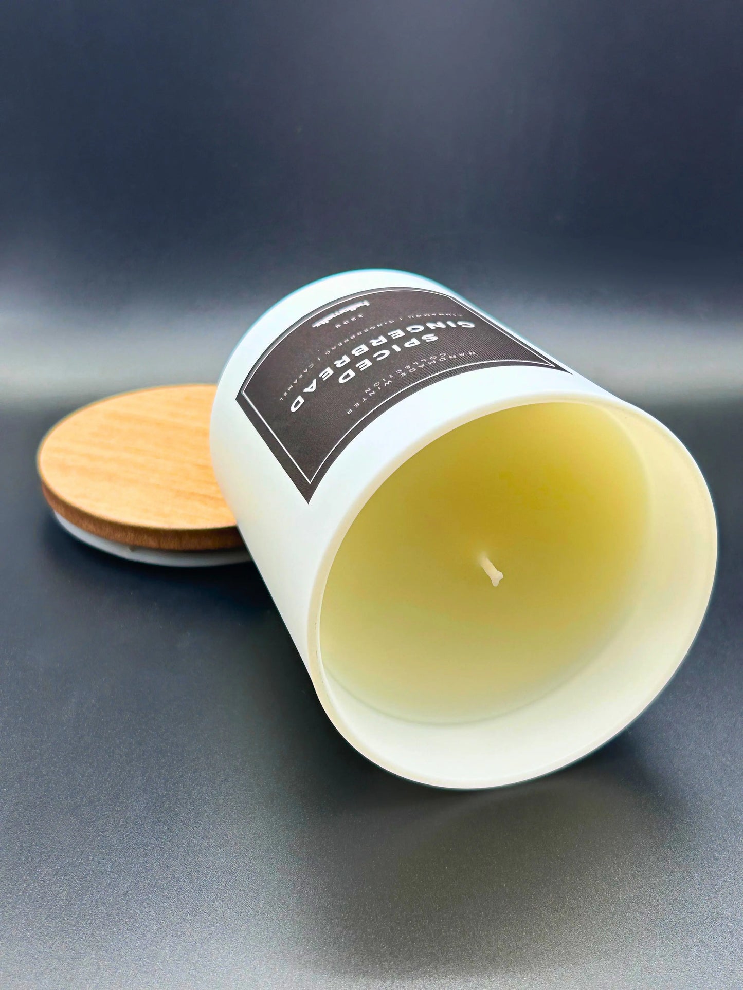 Spiced Gingerbread 220g candle, by Hellomelts, on its side, rich with scents of cinnamon, gingerbread, and caramel, presented in a white matt jar with wooden lid.