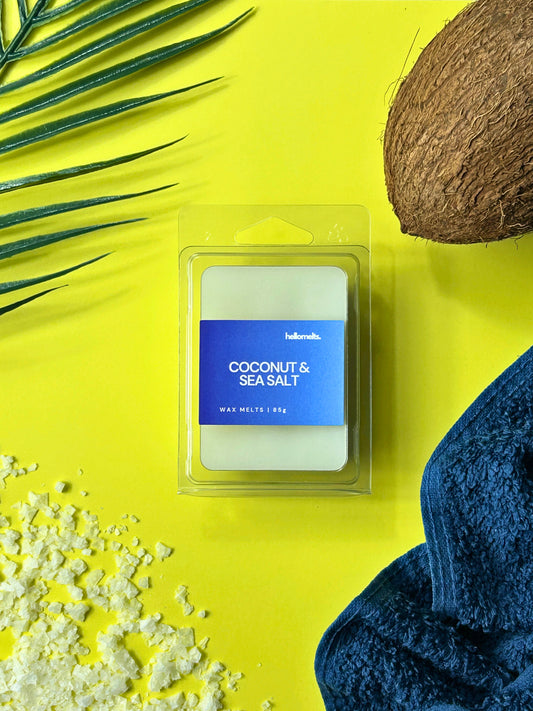 Coconut & Sea Salt wax melts by Hellomelts styled with a coconut shell, sea salt crystals, palm leaves and a blue towel on a bright yellow background