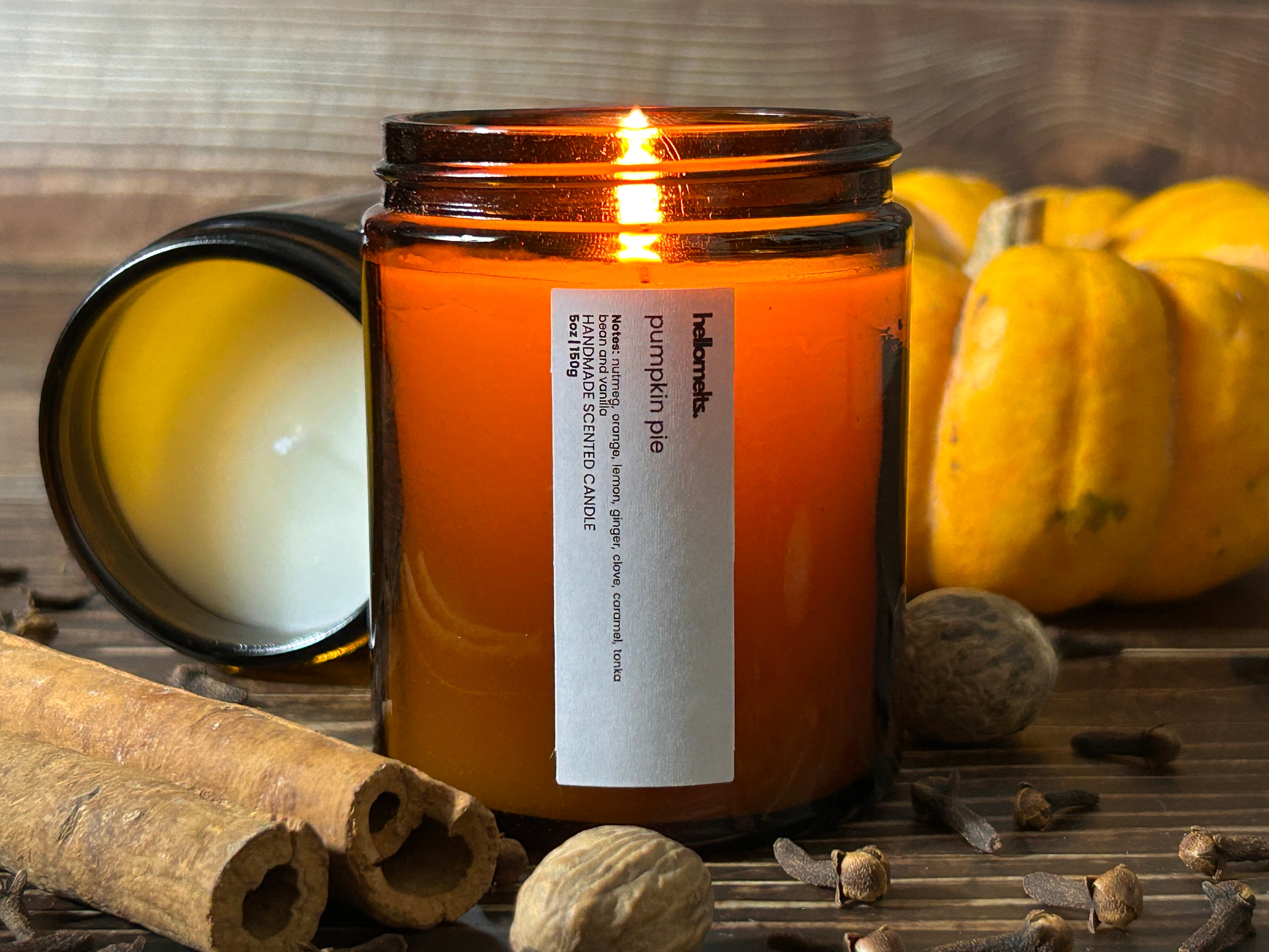 Autumn Collection banner image of a lit Pumpkin Pie candle by Hellomelts, styled with cinnamon sticks, cloves, nutmeg and mini pumpkin on a rustic wooden background