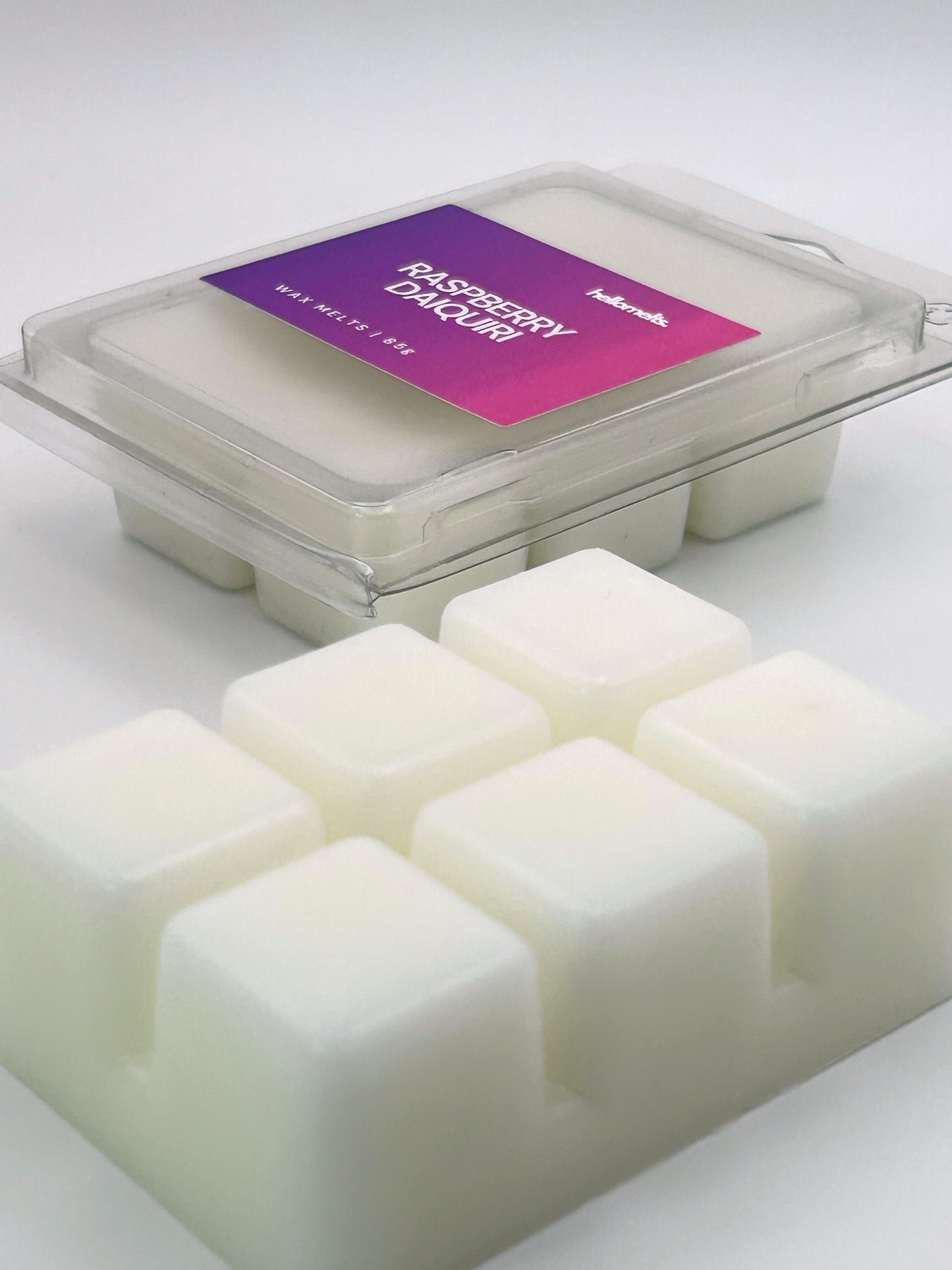 Angled shot of Raspberry Daiquiri 85g wax melt bar in front of its packaging, part of the Summer Collection by Hellomelts