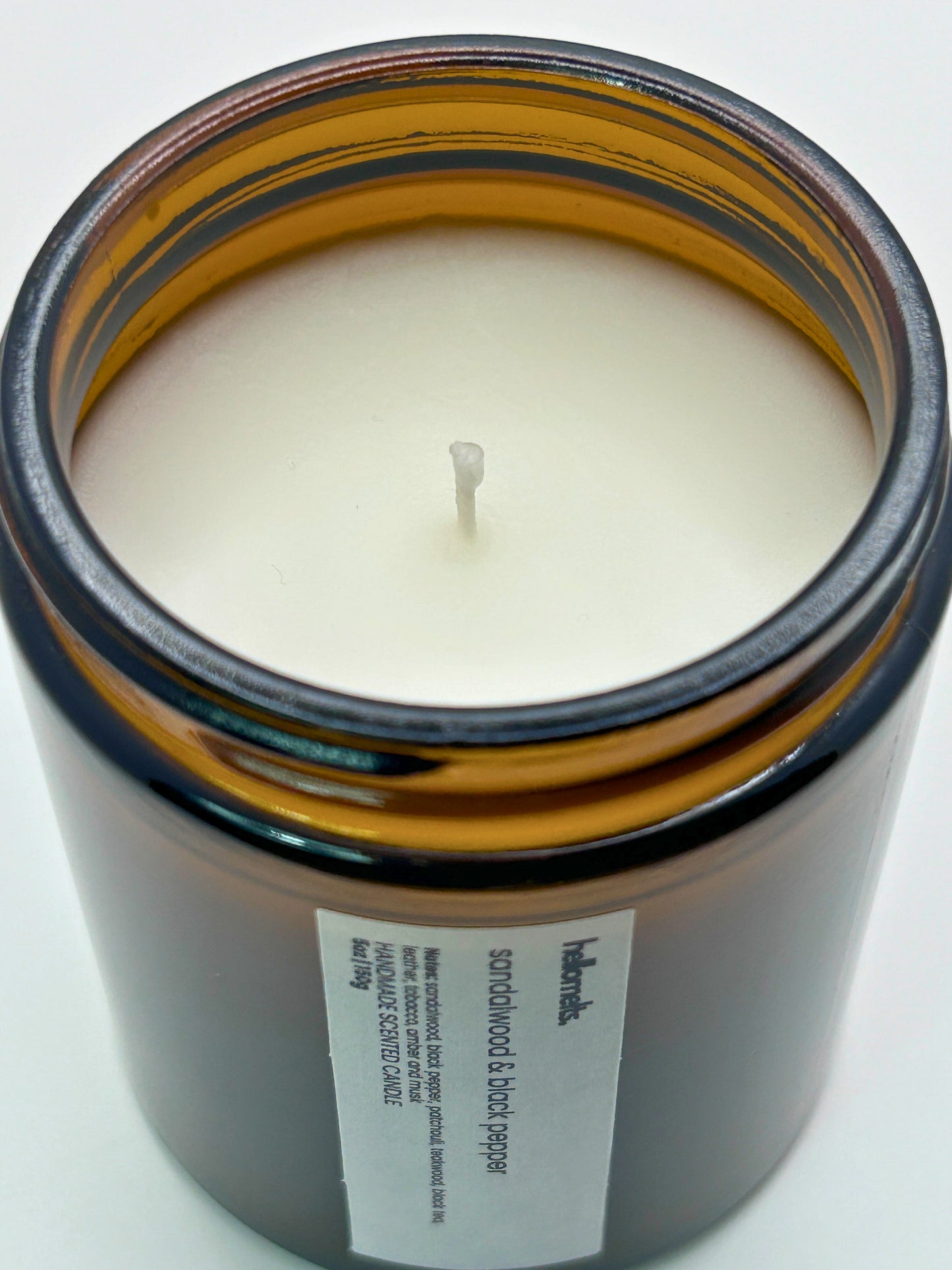 Close-up angled top-down view of Sandalwood & Black Pepper autumn scented candle by Hellomelts, showcasing the smooth wax in an amber jar from the Autumn Collection