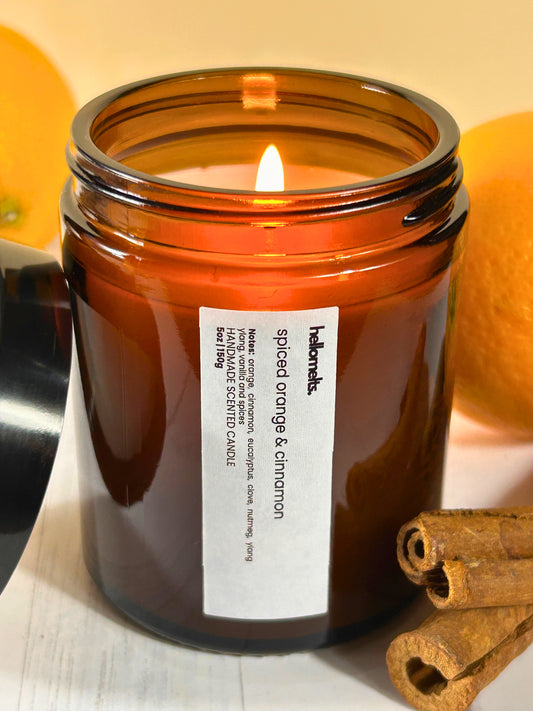 Spiced Orange & Cinnamon candle, lit and burning in an amber glass jar with fresh oranges and cinnamon sticks, handmade by Hellomelts