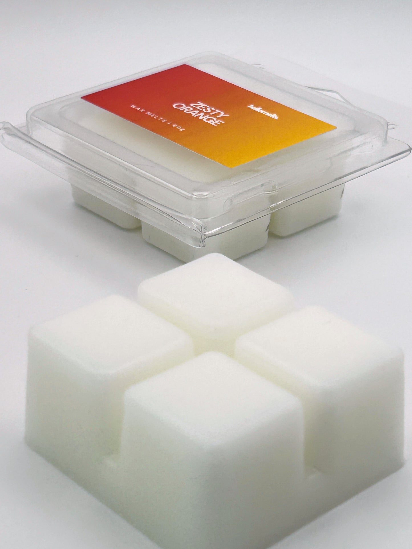 Angled shot of Zesty Orange 60g wax melt bar in front of its packaging, part of the Summer Collection by Hellomelts