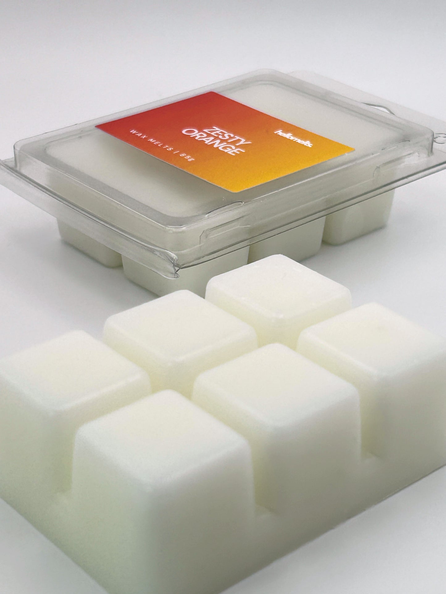 Angled shot of Zesty Orange 85g wax melt bar in front of its packaging, part of the Summer Collection by Hellomelts