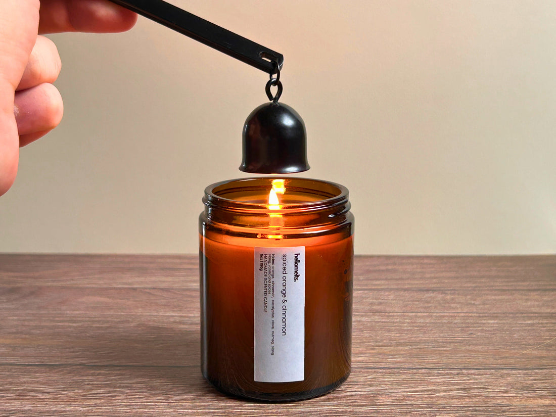 Hand using a black candle snuffer to safely extinguish a lit amber jar candle on a wooden surface