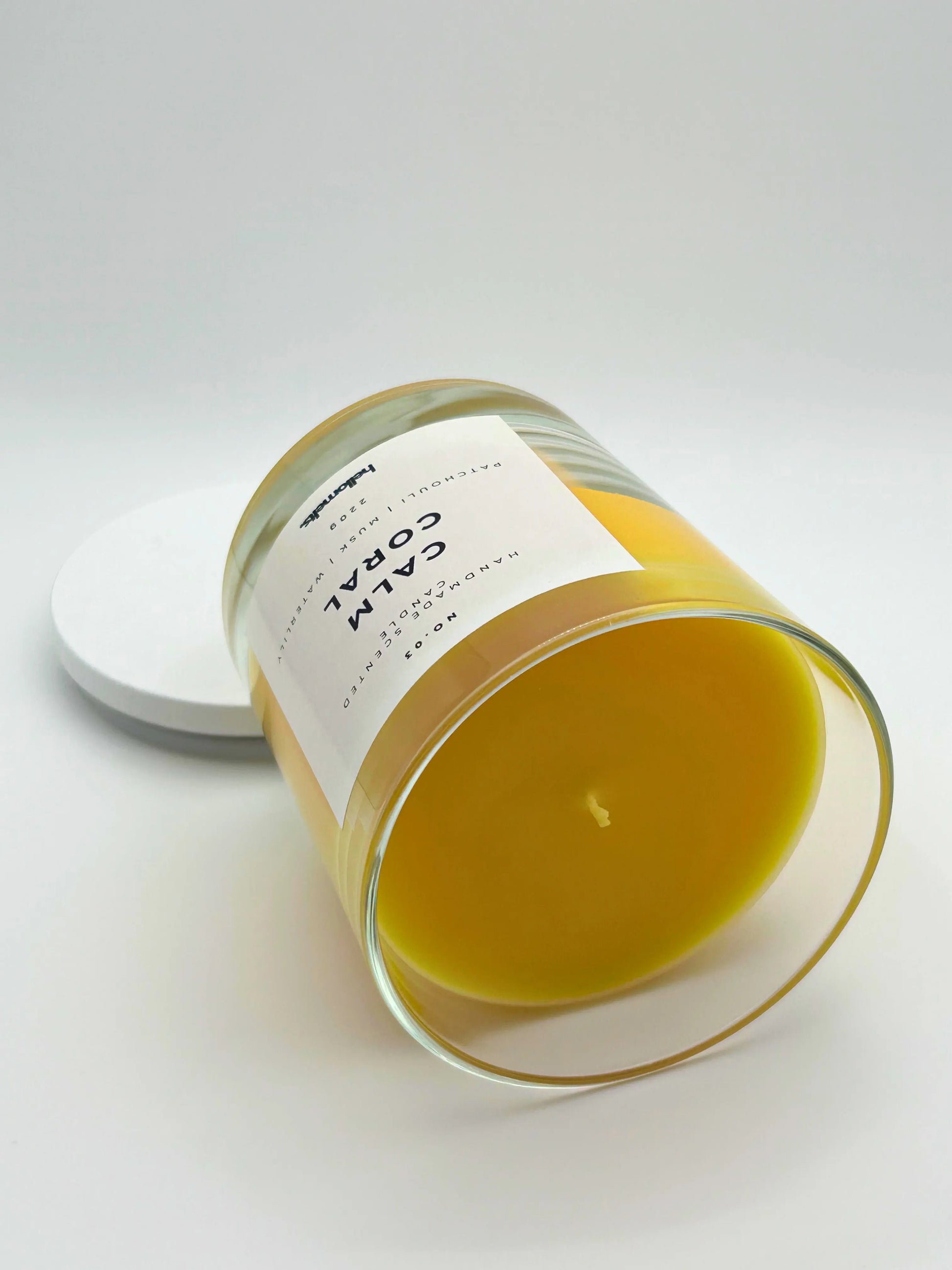 Calm Coral 220g candle, on its side, by Hellomelts, blending patchouli with soothing scents of musk and a touch of waterlily, in a bright yellow wax.