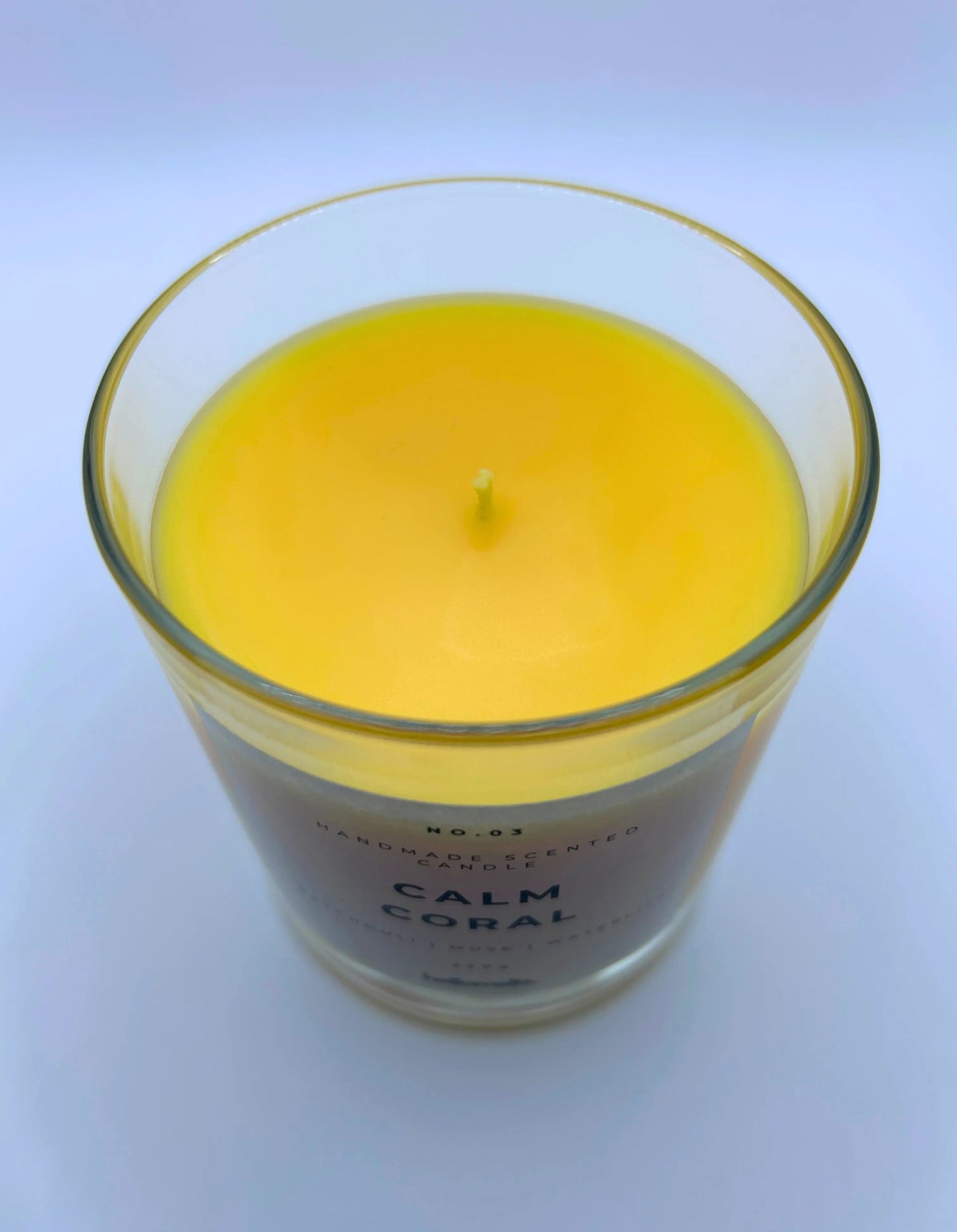 Calm Coral 220g candle, showing top of jar with lid off, by Hellomelts, blending patchouli with soothing scents of musk and a touch of waterlily, in a bright yellow wax.