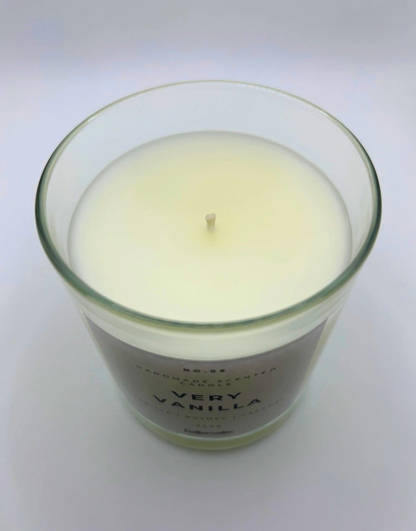 Very Vanilla 220g candle by Hellomelts, showing top of jar with lid off, infused with the warm scents of vanilla, nutmeg, and caramel, showcased in a simple white wax.