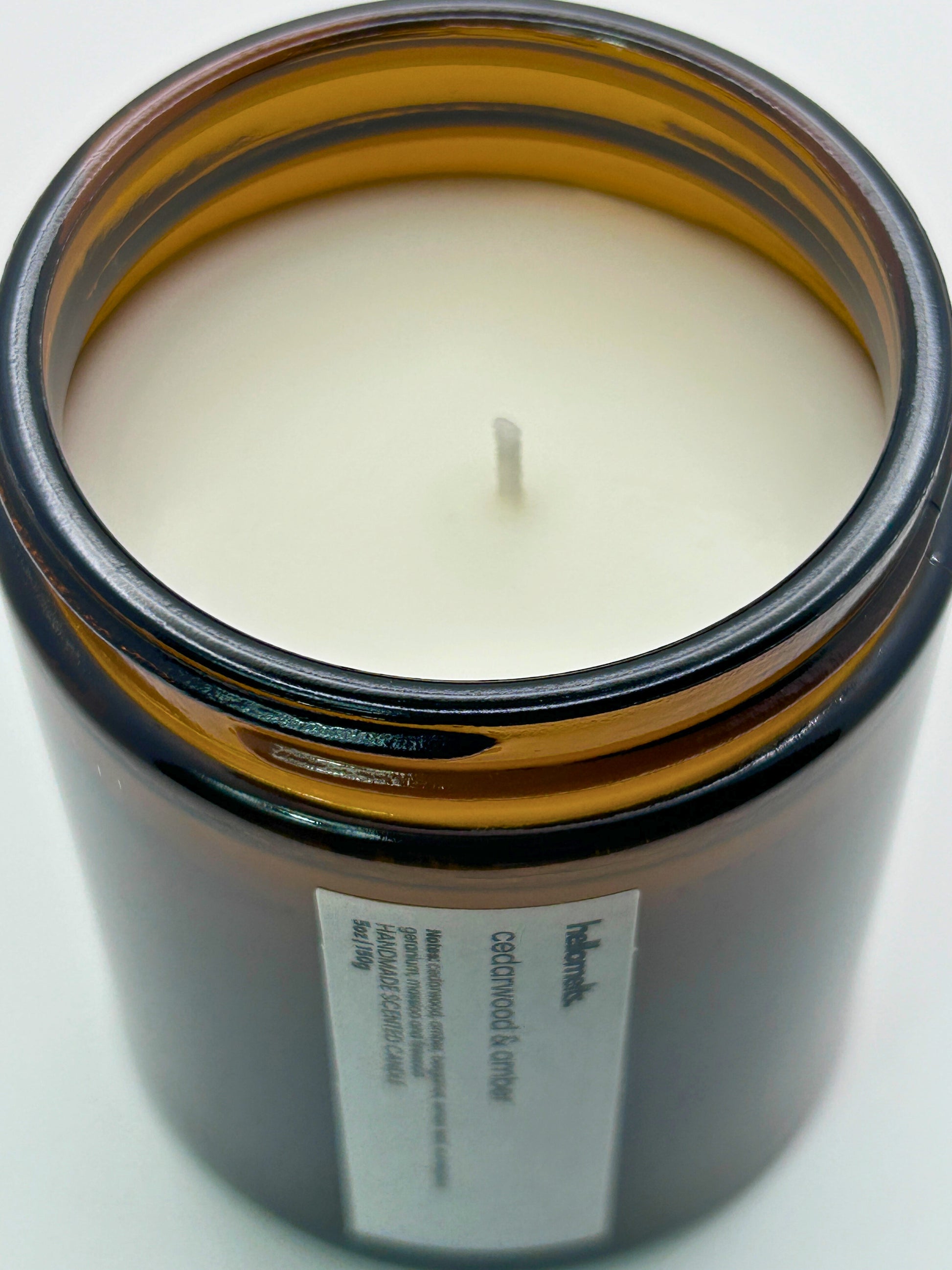 Close-up angled top-down view of Cedarwood &  Amber autumn scented candle by Hellomelts, showcasing the smooth wax in an amber jar from the Autumn Collection
