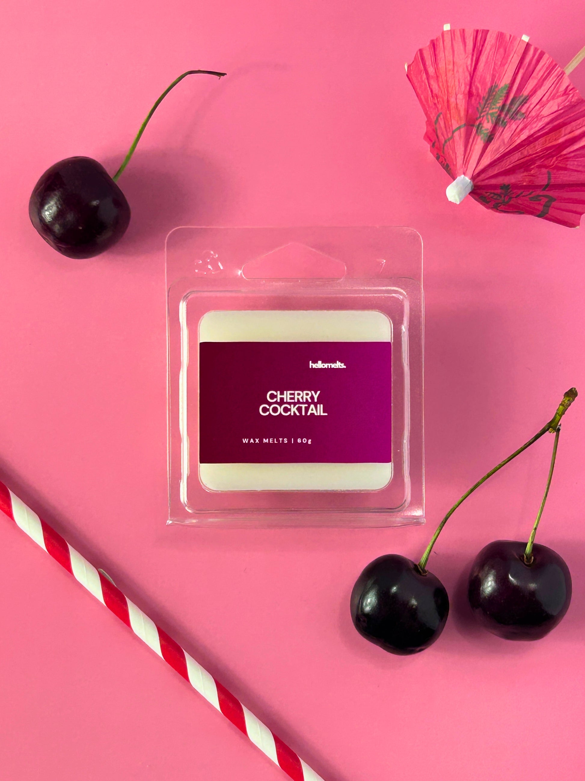Cherry Cocktail wax melts by Hellomelts shown in clear clamshell packaging on a pink background styled with fresh cherries, a striped straw, and a cocktail umbrella, photographed for the Summer Collection