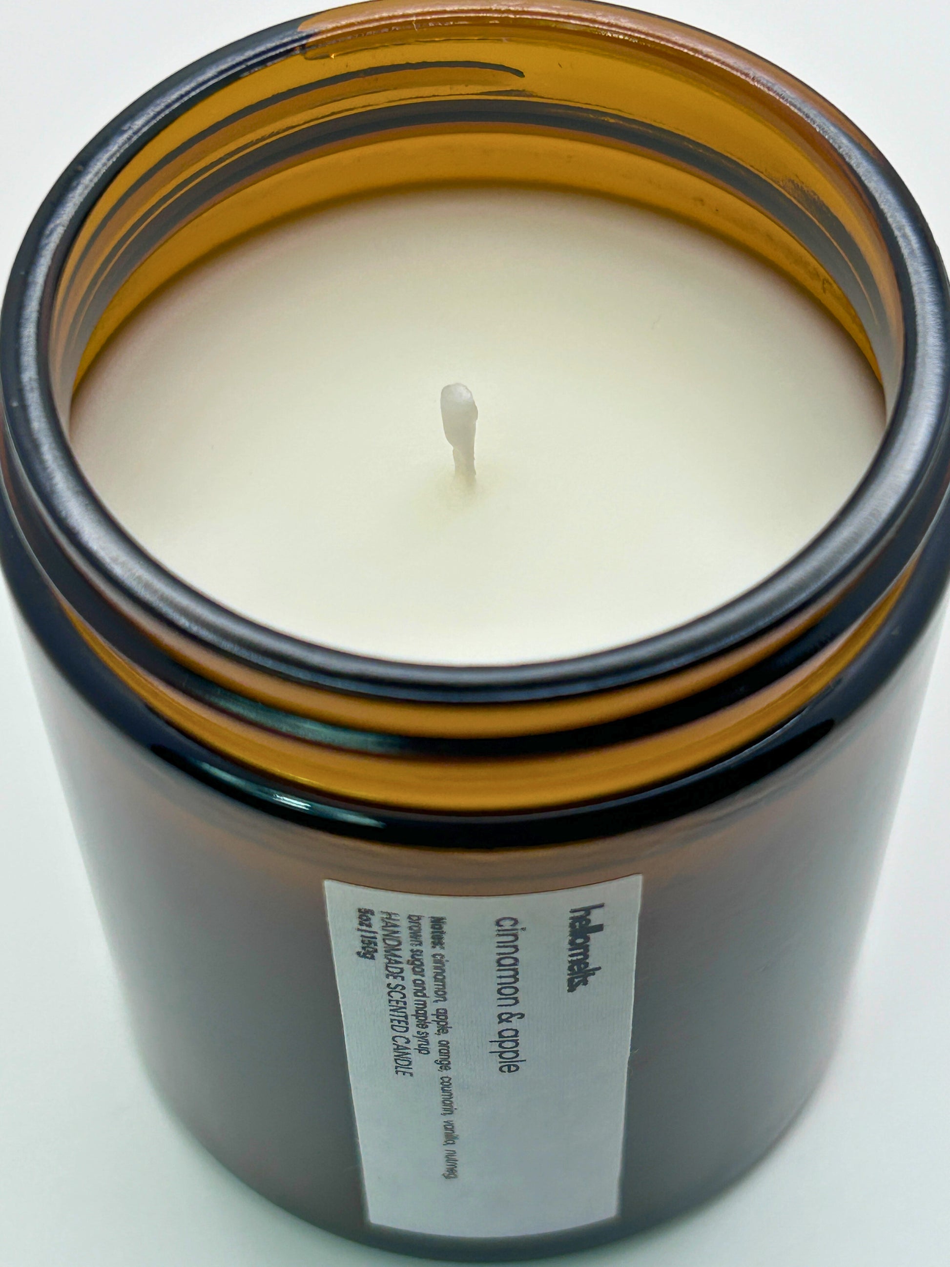 Close-up angled top-down view of Cinnamon & Apple autumn scented candle by Hellomelts, showcasing the smooth wax in an amber jar from the Autumn Collection