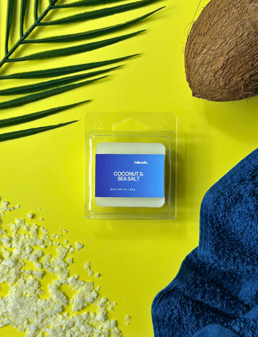 Coconut & Sea Salt wax melts by Hellomelts styled with a coconut shell, sea salt crystals, palm leaves and a blue towel on a bright yellow background