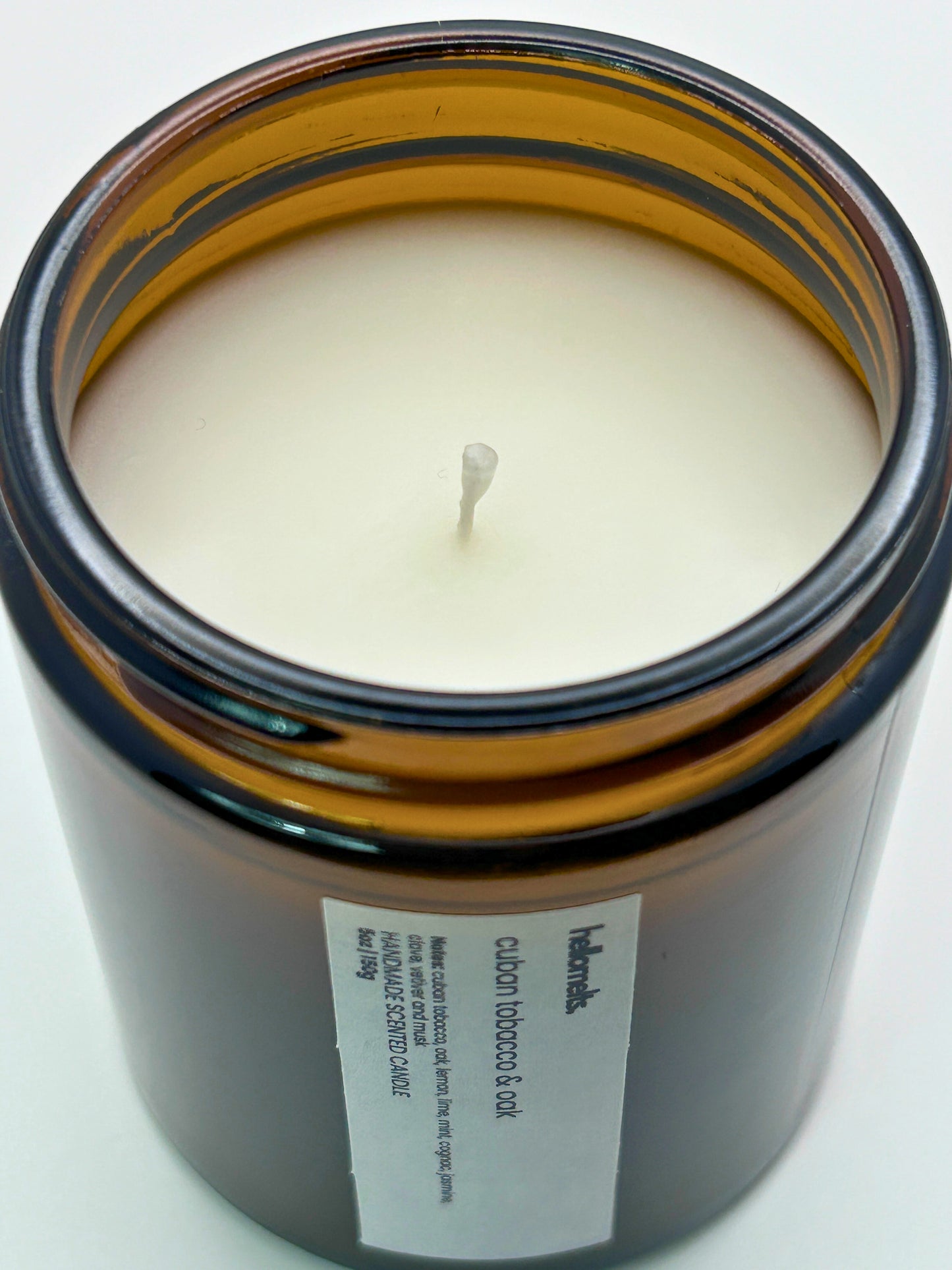 Close-up angled top-down view of Cuban Tobacco & Oak autumn scented candle by Hellomelts, showcasing the smooth wax in an amber jar from the Autumn Collection