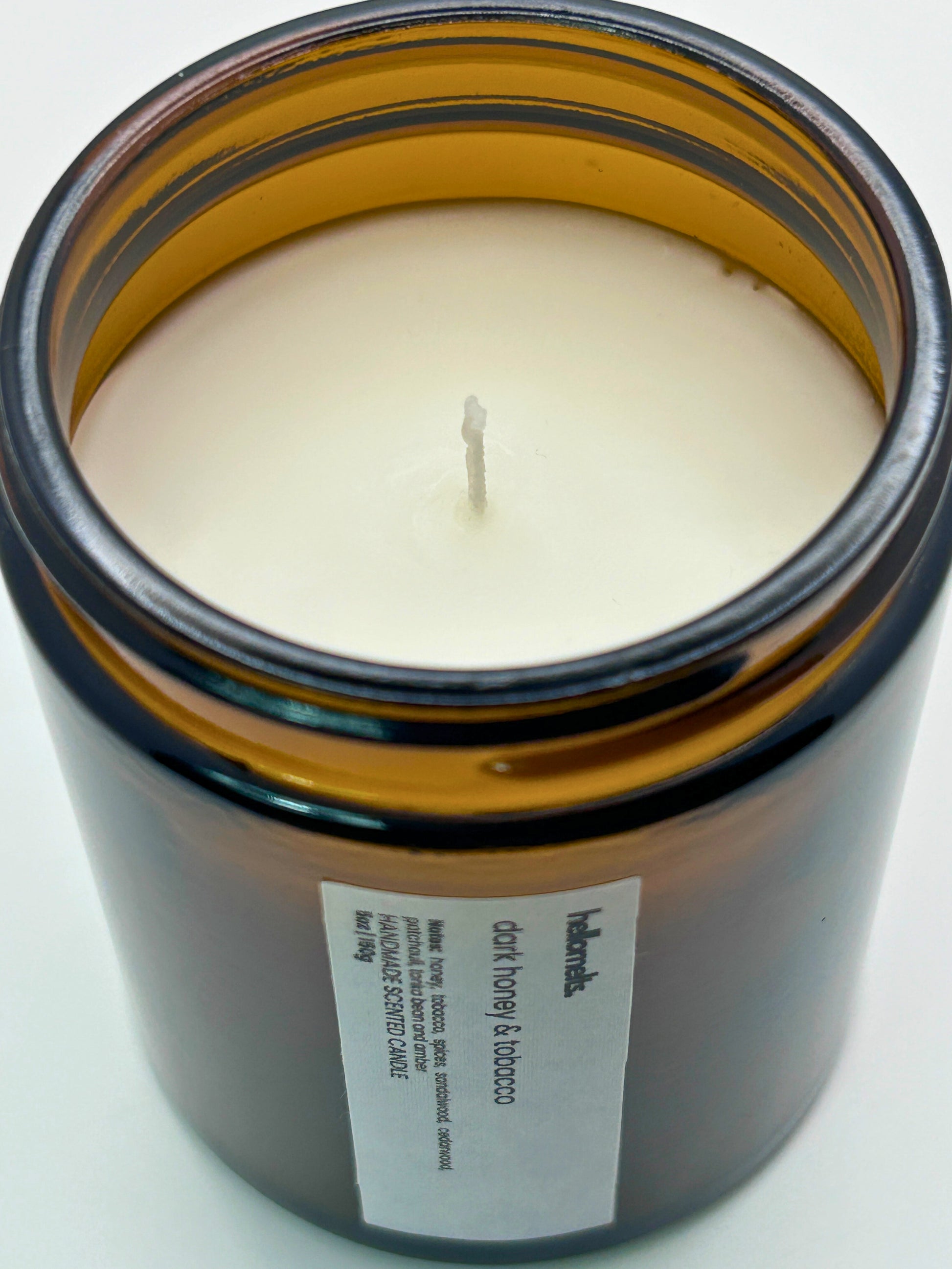 Close-up angled top-down view of Dark Honey & Tobacco autumn scented candle by Hellomelts, showcasing the smooth wax in an amber jar from the Autumn Collection