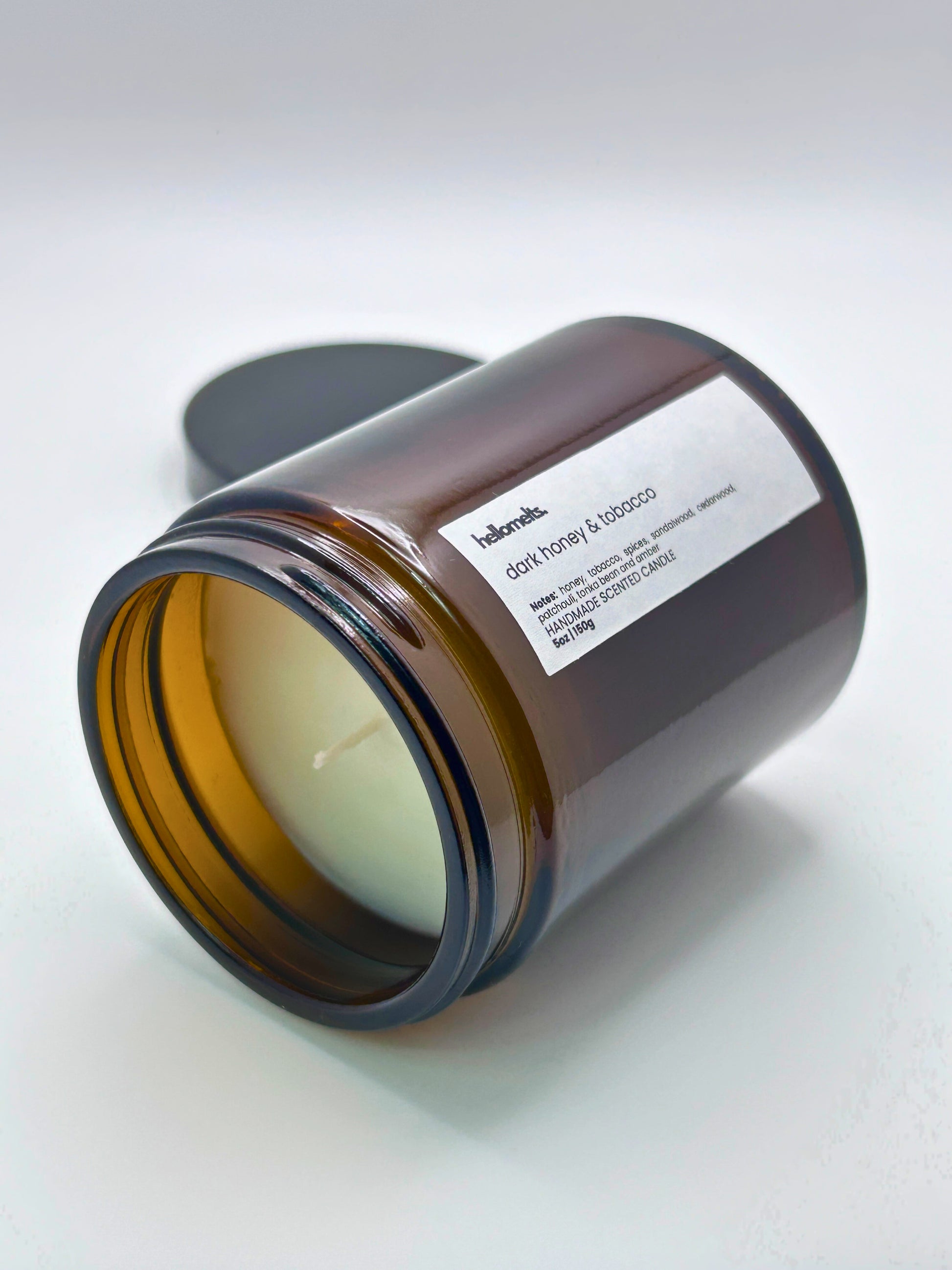 Dark Honey & Tobacco autumn scented candle by Hellomelts lying on its side with the wick facing forward, part of the Autumn Collection