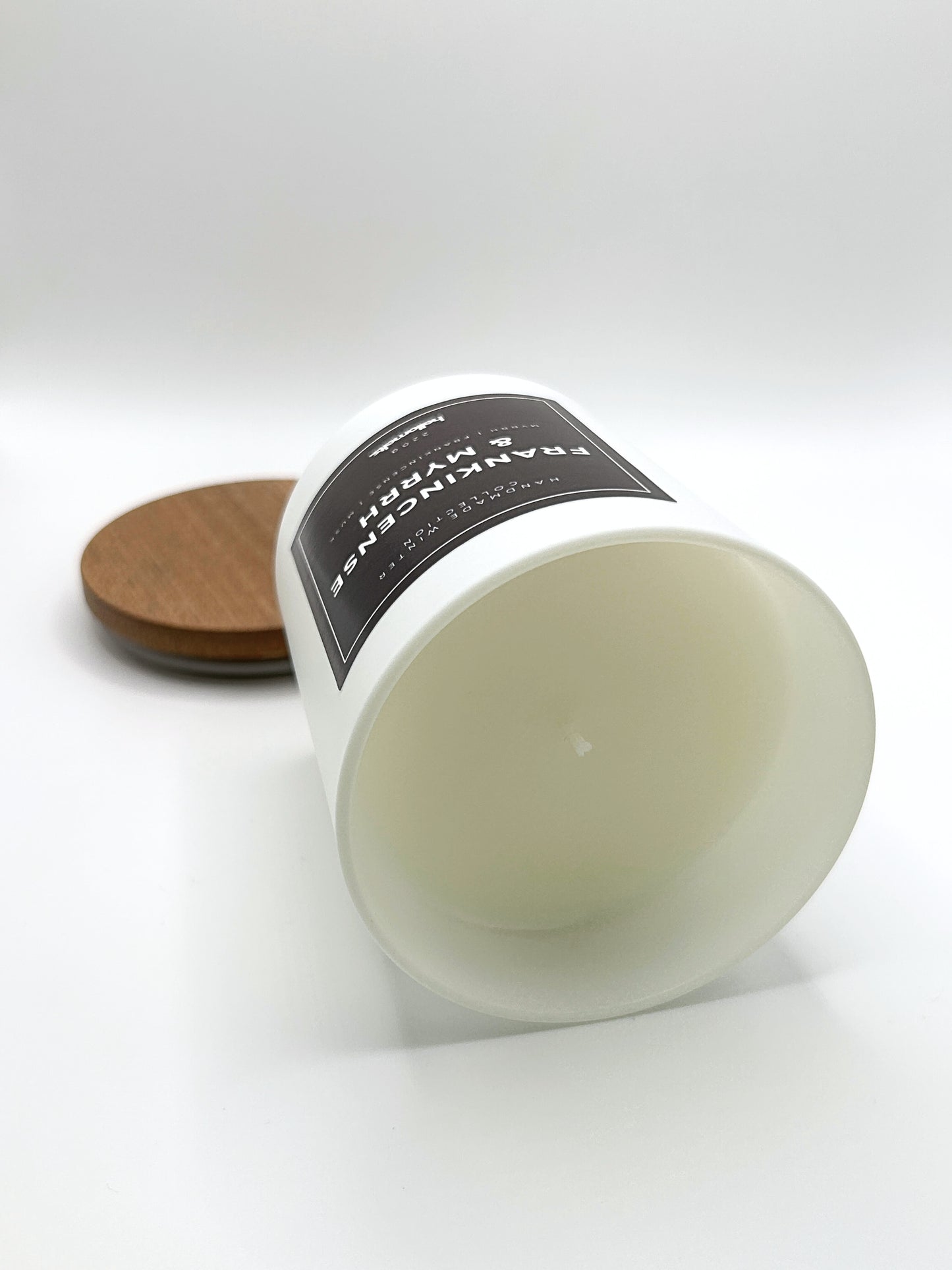 Frankincense & Myrrh 220g candle laid on its side with the lid in the background, showing the matte white jar from the Hellomelts Winter Collection