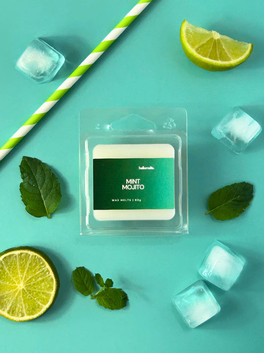 Mint Mojito wax melt bar by Hellomelts, displayed in clear clamshell packaging with mint leaves, lime wedges and ice cubes on a bright turquoise background as part of the Summer Collection