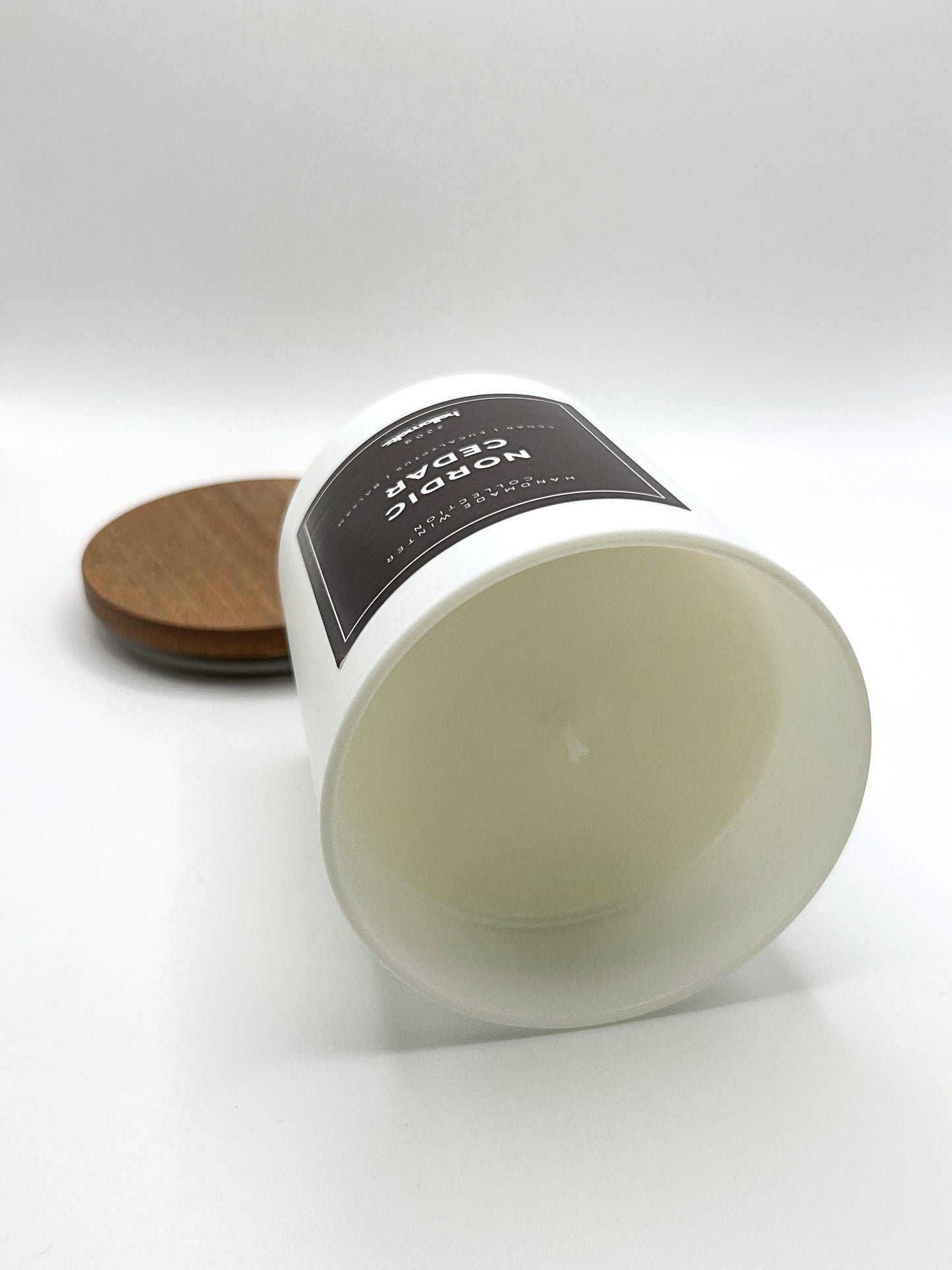 Nordic Cedar 220g candle laid on its side with the lid in the background, showing the matte white jar from the Hellomelts Winter Collection