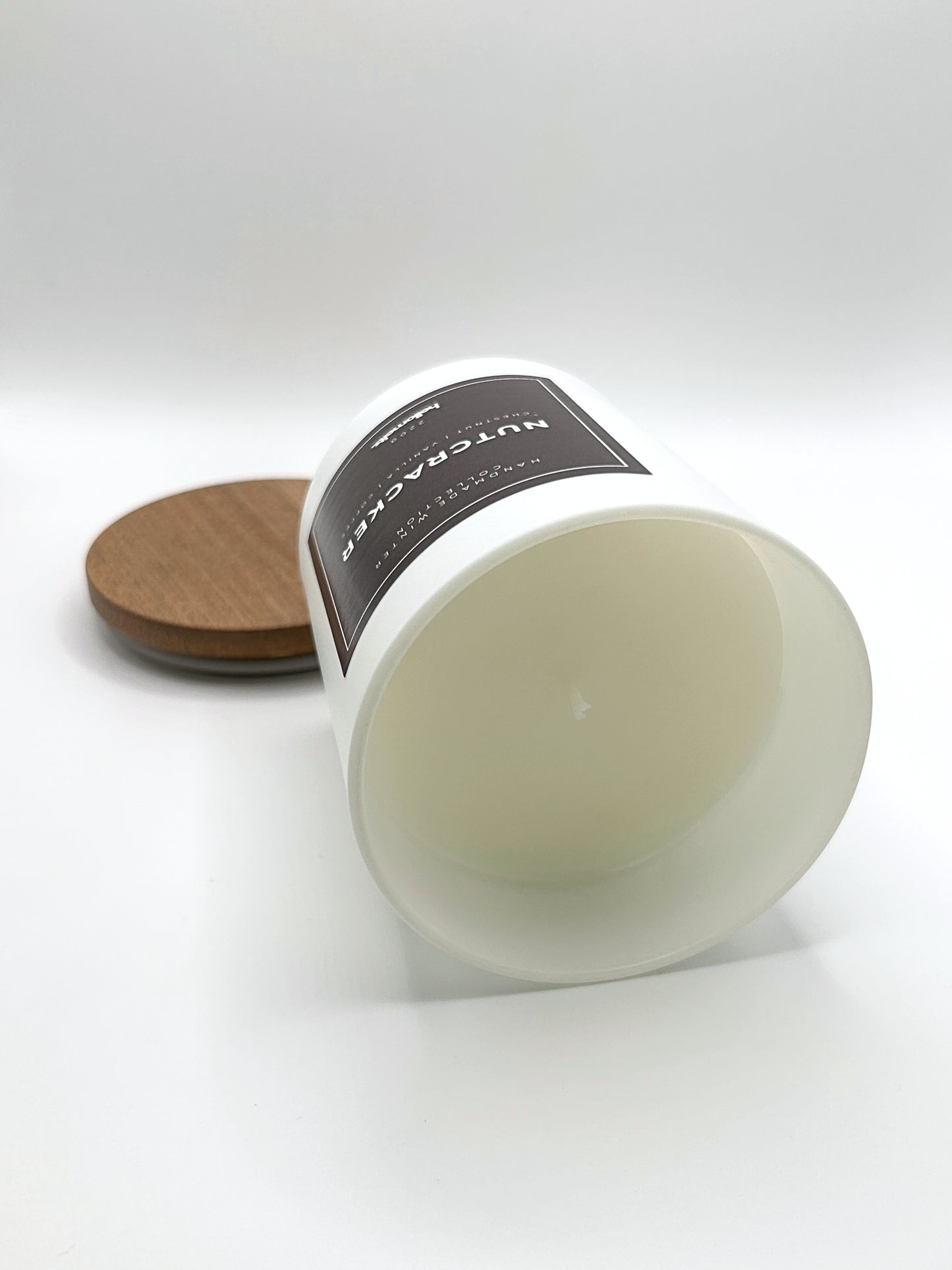 Nutcracker 220g candle laid on its side with the lid in the background, showing the matte white jar from the Hellomelts Winter Collection