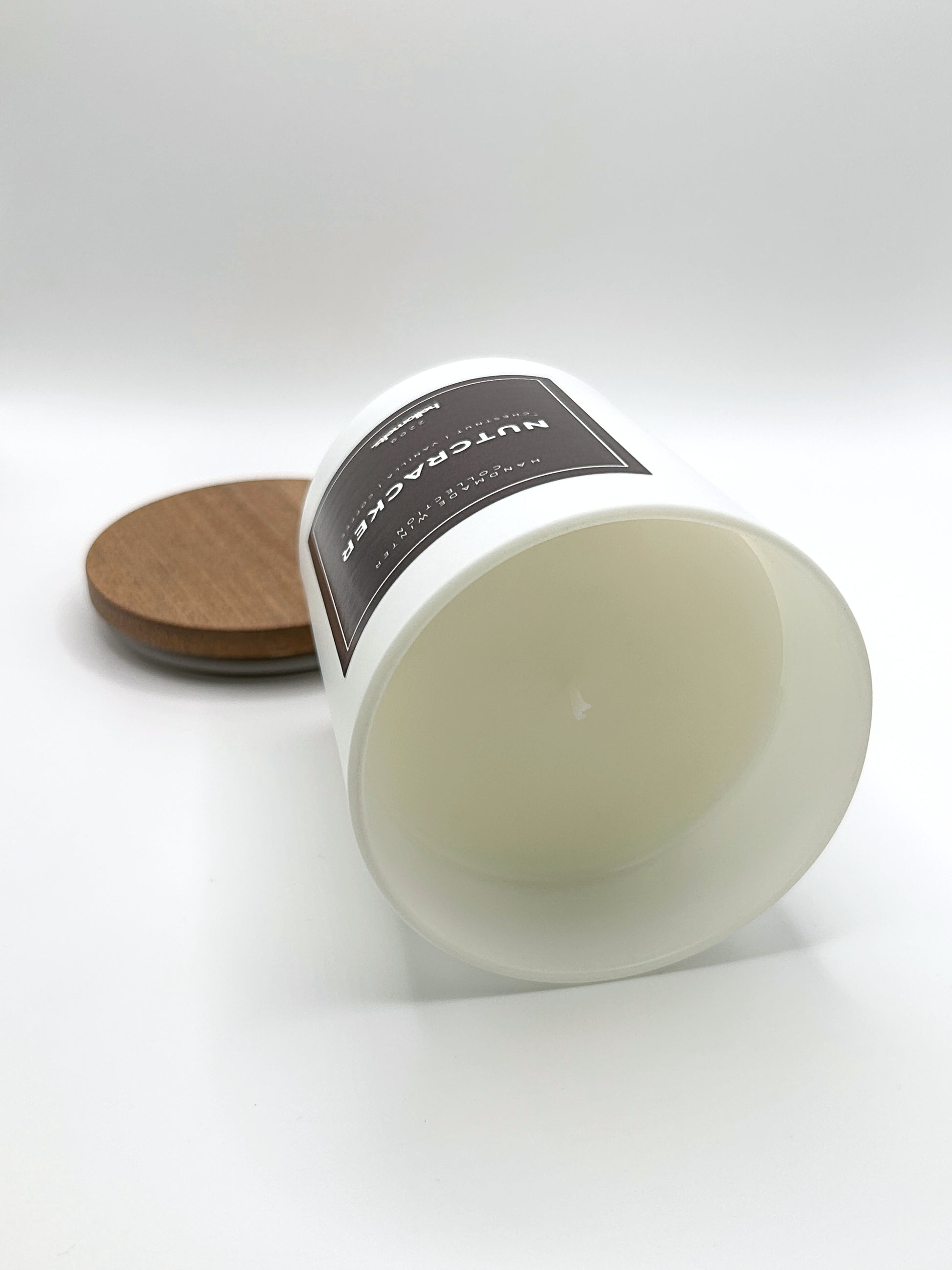 Nutcracker 220g candle laid on its side with the lid in the background, showing the matte white jar from the Hellomelts Winter Collection