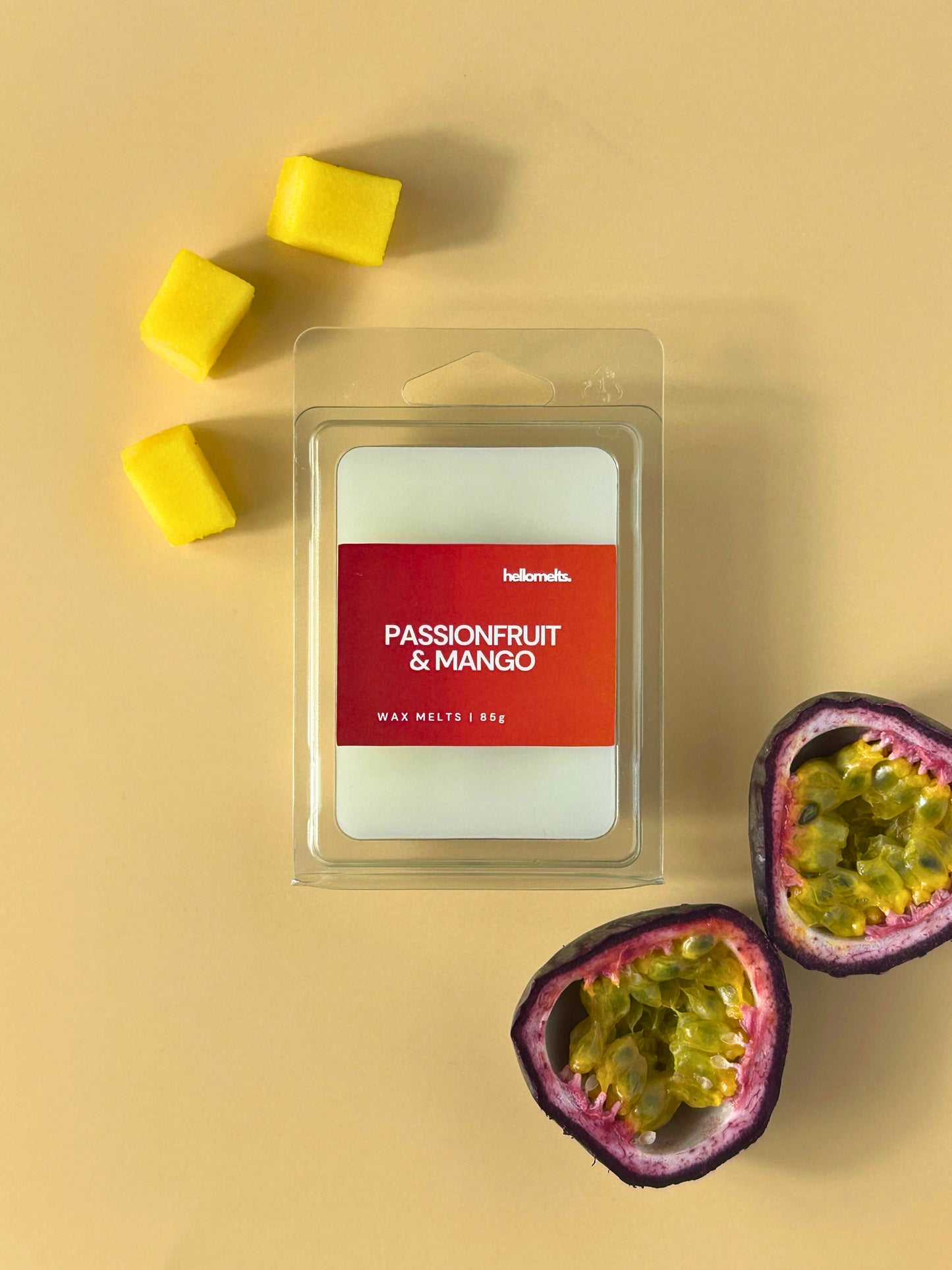 Passionfruit & Mango wax melts by Hellomelts, shown in clear clamshell packaging on a warm neutral background with fresh passionfruit halves and mango cubes, from the Summer Collection