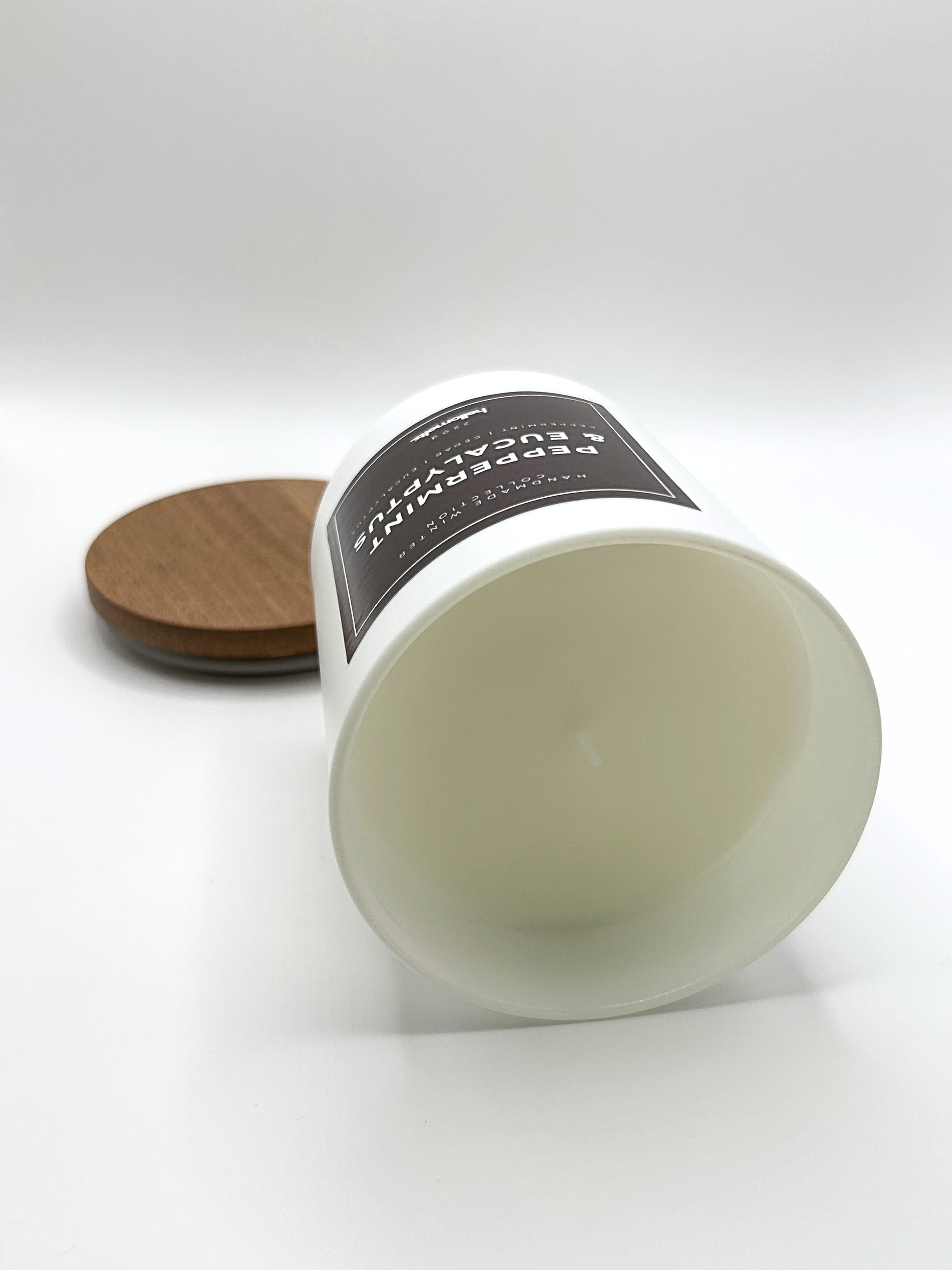Peppermint & Eucalyptus 220g candle laid on its side with the lid in the background, showing the matte white jar from the Hellomelts Winter Collection