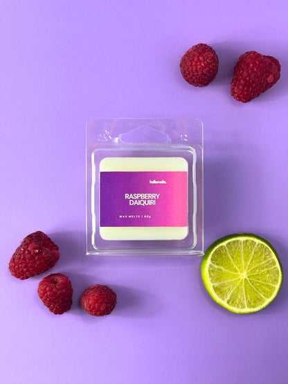 Raspberry Daiquiri wax melt bar in clear clamshell packaging, styled with fresh raspberries and sliced lime on a purple background, Hellomelts Summer Collection