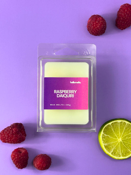 Raspberry Daiquiri wax melt bar in clear clamshell packaging, styled with fresh raspberries and sliced lime on a purple background, Hellomelts Summer Collection