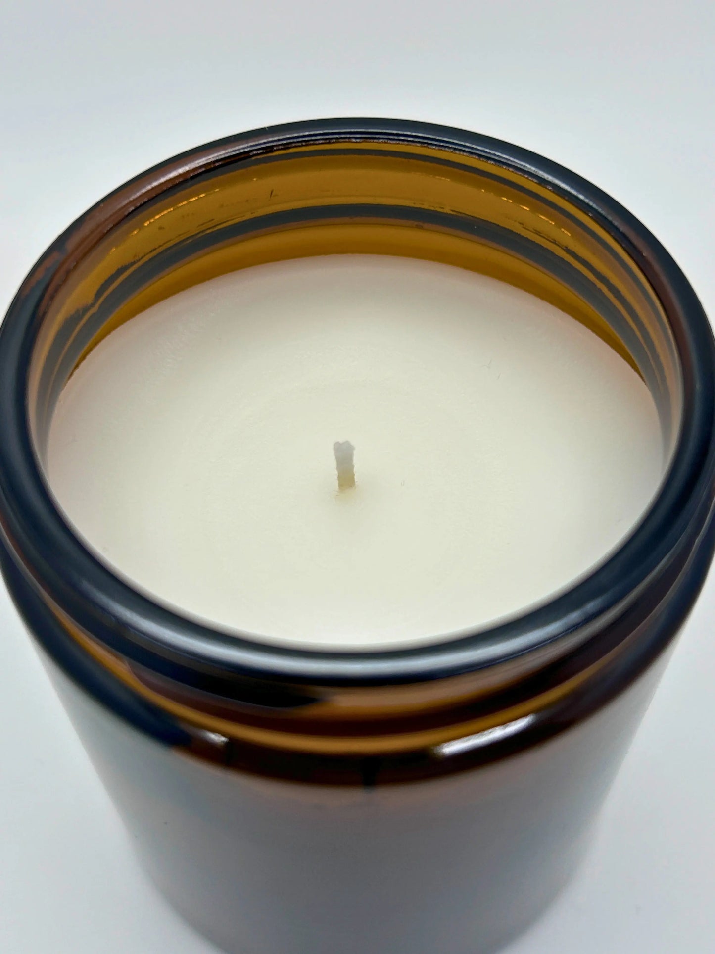 Close-up angled top view of Sandalwood & Black Pepper candle by Hellomelts, showcasing the smooth wax in an amber jar from the autumn collection.