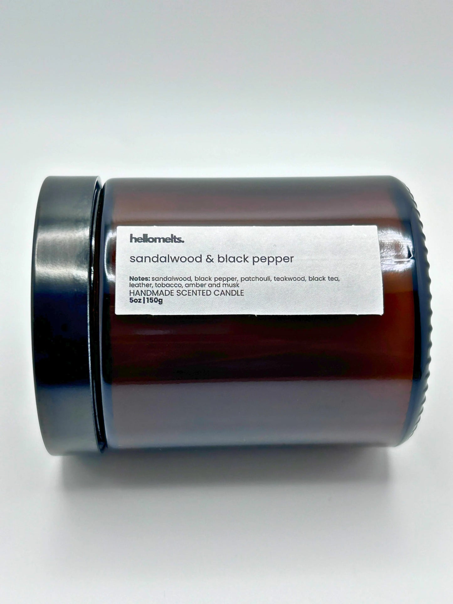 Close-up of Sandalwood & Black Pepper candle by Hellomelts lying down with the lid on, part of the autumn collection.