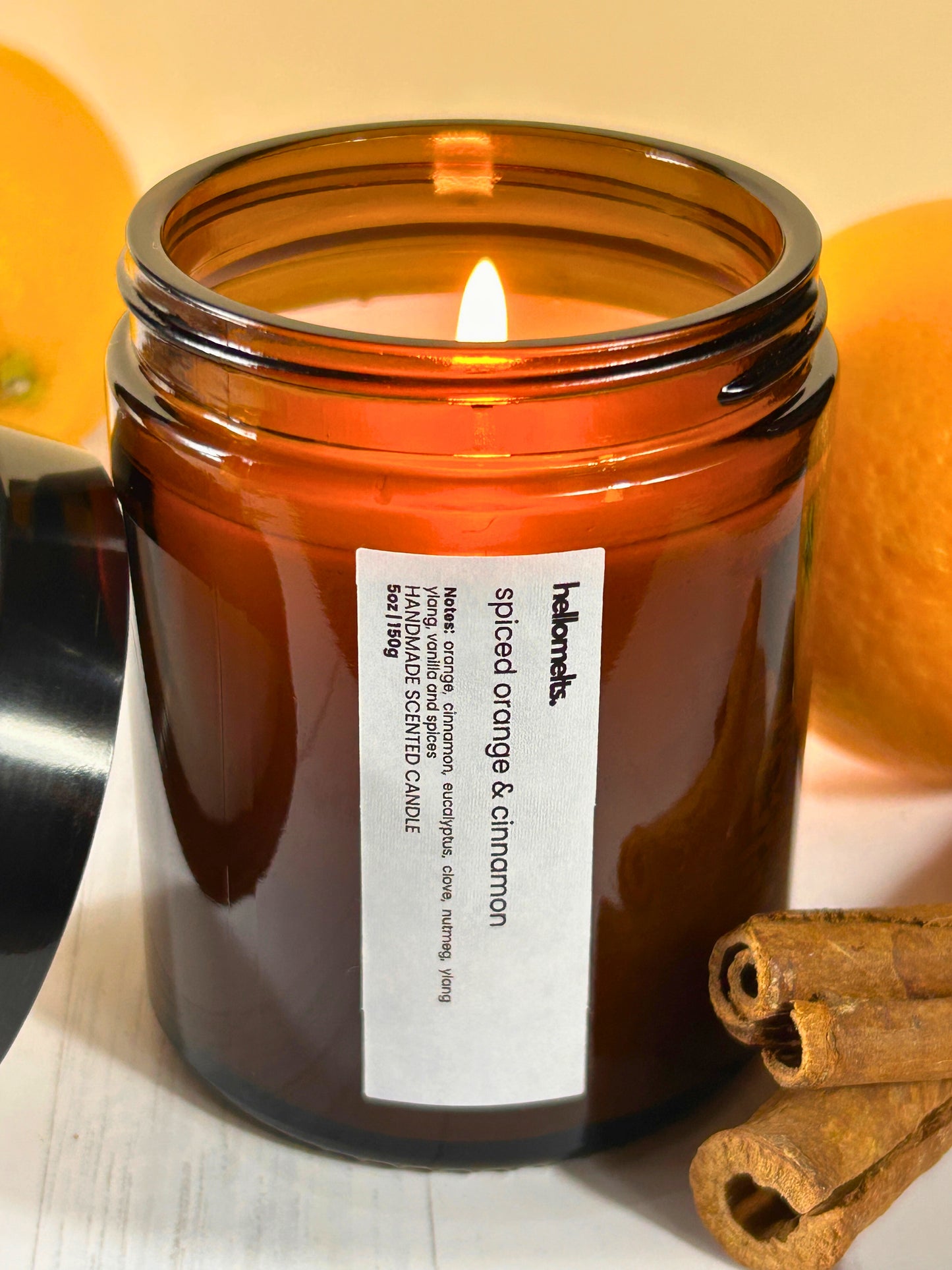 Spiced Orange & Cinnamon candle, lit and burning in an amber glass jar with fresh oranges and cinnamon sticks, handmade by Hellomelts