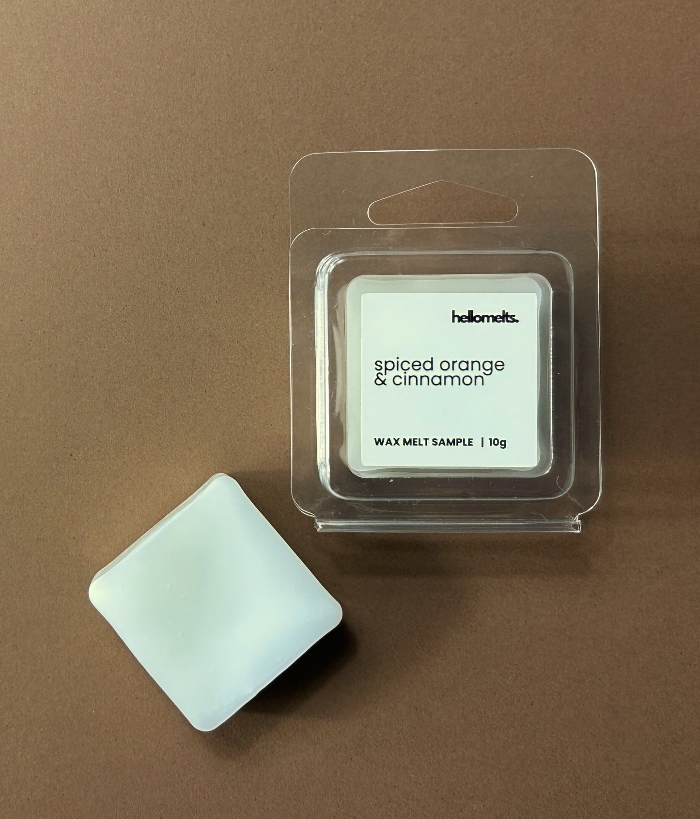 Hellomelts Spiced Orange & Cinnamon free 10g wax melt sample in clear clamshell packaging with melt beside it, styled on a brown background as part of the Autumn Collection