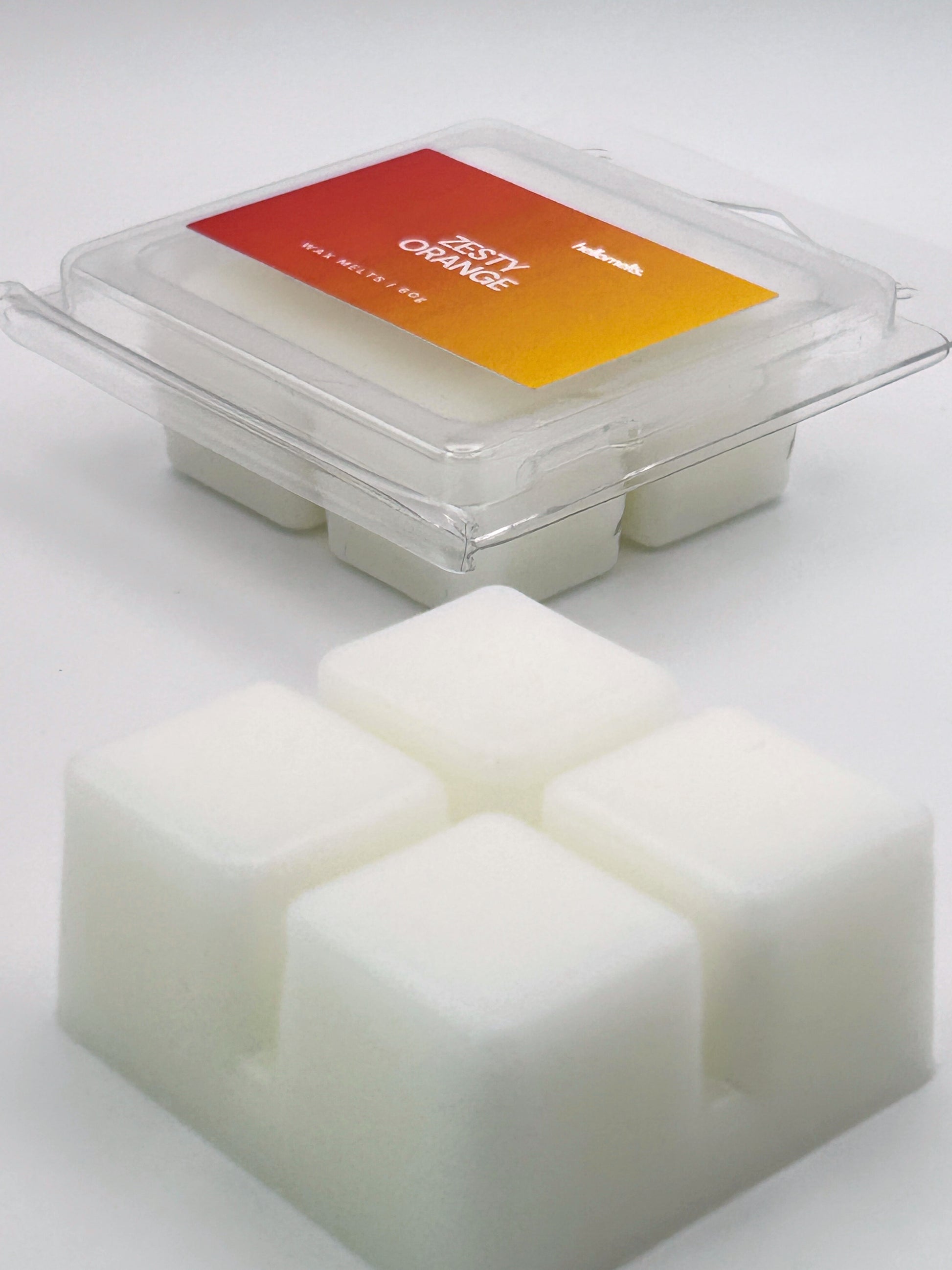 Angled shot of Zesty Orange 60g wax melt bar in front of its packaging, part of the Summer Collection by Hellomelts
